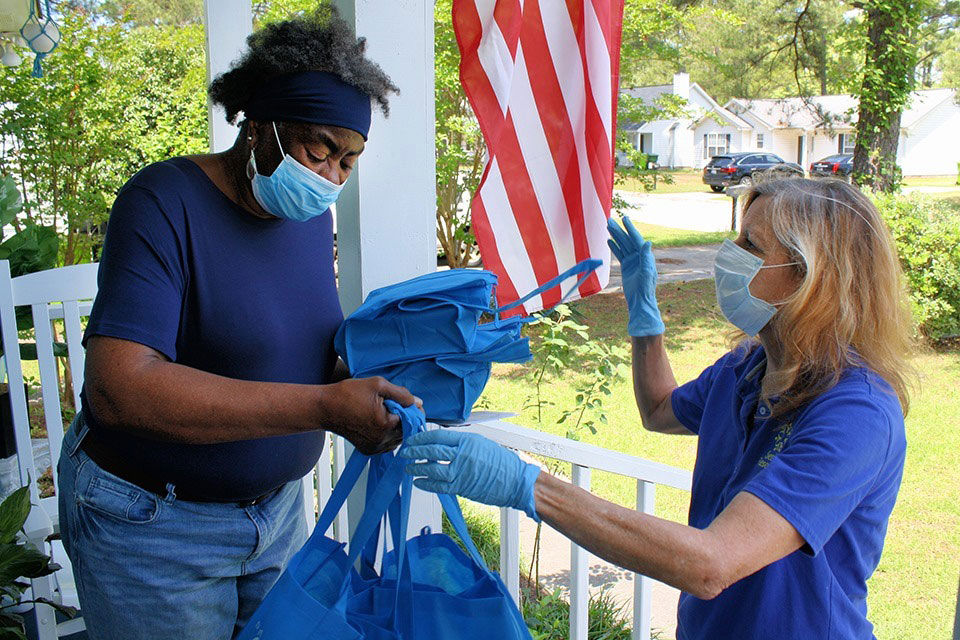 BlueCross employee hands meals to elderly woman on front porch