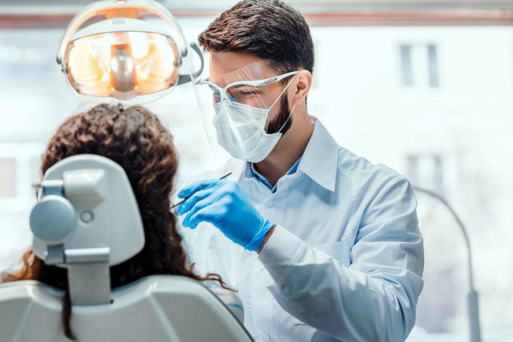 Dentist works on patient with mask and face shield