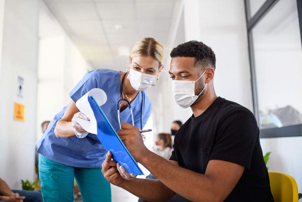 man wearing mask fills out paperwork with doctor wearing mask