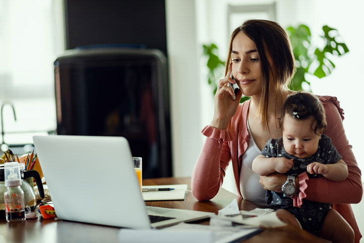 woman holding baby talking on phone and looking at computer