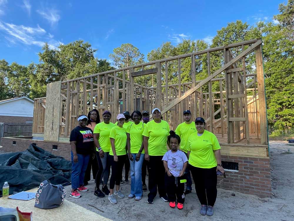 group of people wearing bright shirts in front of unfinished house