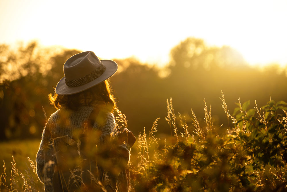 woman in hat looking off into sunrise in field